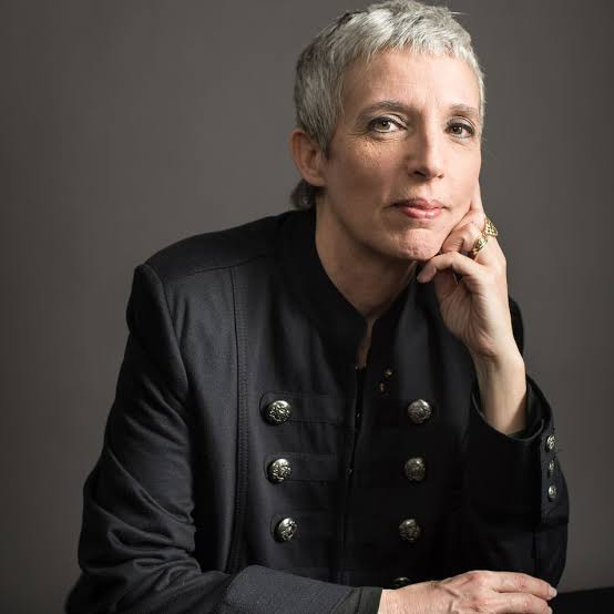 Portrait of Nathalie Cabrol, seated with chin resting on hand, wearing a dark buttoned jacket.